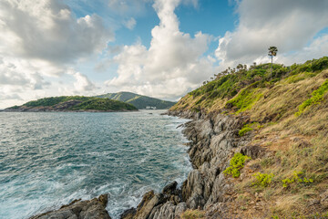 Waves hit the rocky shore on the Promthep cape with high palm trees in the sunset lights