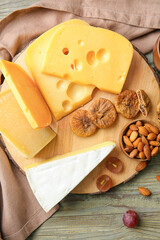 Board with tasty cheese, nuts and dried figs on wooden background, closeup