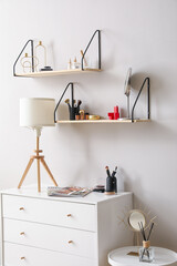 Shelves with decorative cosmetics and chest of drawers near light wall
