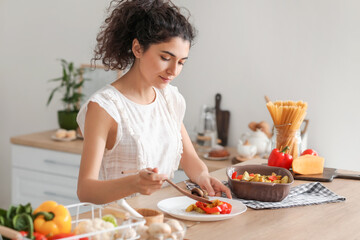 Young woman putting tasty dish on plate in kitchen