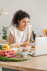 Young woman using laptop while eating in kitchen