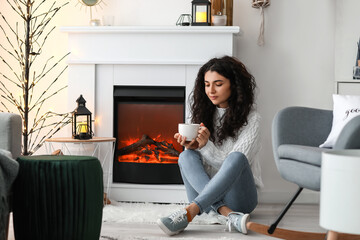 Beautiful woman drinking tea near fireplace at home
