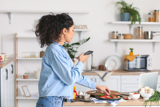 Young woman taking photo of tasty pizza in kitchen