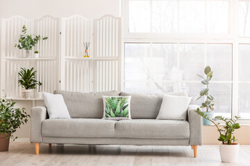 Cozy sofa with houseplants and folding screen near window in room