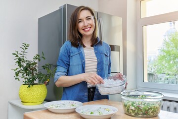 Smiling woman in kitchen near refrigerator with ice for cooling food