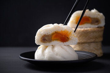 Steamed bun stuffed with minced pork and salted egg yolk eating by chopsticks on black background, Asian food