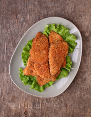 Traditional chicken schnitzel on a plate with lettuce on an old wooden background. Top view.