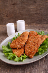 Traditional chicken schnitzel on a plate with lettuce on an old wooden background.