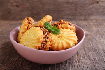 Sandwich cookies with condensed milk and nuts decorated with mint in a plate on an old wooden background.