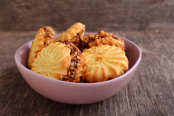 Sandwich cookies with condensed milk and nuts in a plate on an old wooden background.
