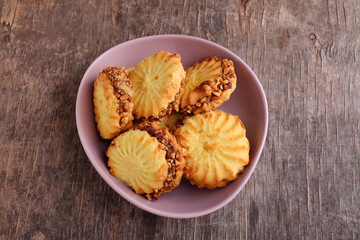 Sandwich cookies with condensed milk and nuts in a plate on an old wooden background, top view.