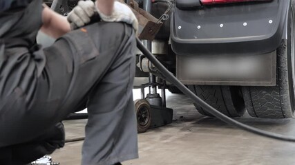 A mechanic at the lorry service station lifted up the truck rear axle with a pneumatic jack and disconnects the air hose