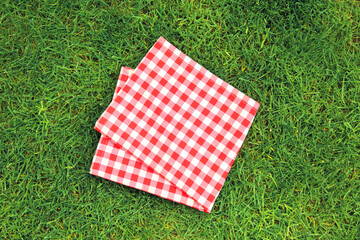 Red picnic folded towel on green grass top view, checked cloth flat lay. Food advertisement display.