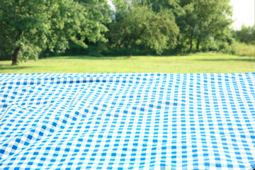 Blue checkered blanket on grass field natural background. Food advertisement display. Picnic cloth lying down outdoors.