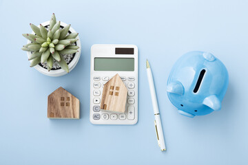Saving for house concept, House model on calculator with piggy bank on blue background - obrazy, fototapety, plakaty