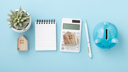 Calculator with house model, notebook and piggy bank