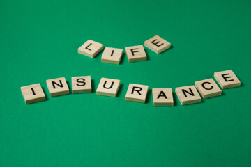 Words life insurance by wooden blocks on green background.