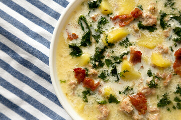 Homemade Zuppa Toscana with Kale and Bread in a white bowl, top view. Flat lay, overhead, from above. Close-up.