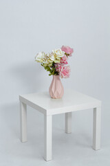 Pink vase with flowers on the table on a white background. Space for text. Close-up.	