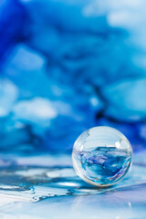 A transparent glass ball on an abstract blue background. The technique of alcoholic ink. Copy space.
