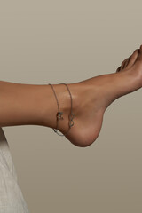 Cropped shot of female bare foot in the air. The ankle is adorned with silver anklet made as double-row chain with charms shaped as infinity sign, heart and letter N.