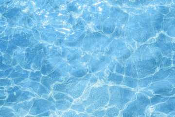 Blue, light pool water outside. Water texture on a sunny day, top view. Ripples and glare on the swimming pool surface. Natural liquid background