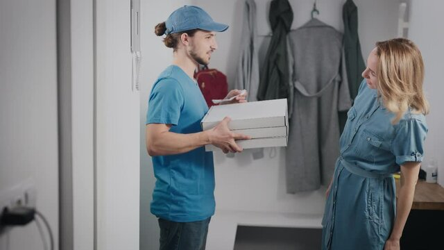 Young food delivery man in a blue uniform. A man brought pizza and a bag of food to a beautiful woman.