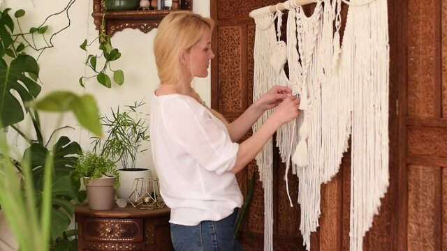 Attractive blonde woman weaving macrame from light threads in a home workshop.Handmade concept.Slow motion.