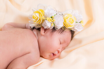 Obraz na płótnie Canvas Portrait of a one month old sleeping, newborn baby girl. She is wearing a flower crown and sleeping on a cream blanket. Concept portrait studio fashion newborn.