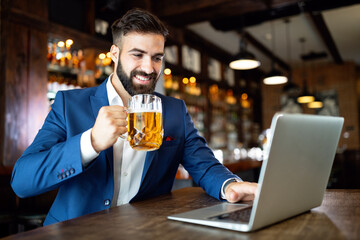 Happy businessman raising glass of beer after work in a pub