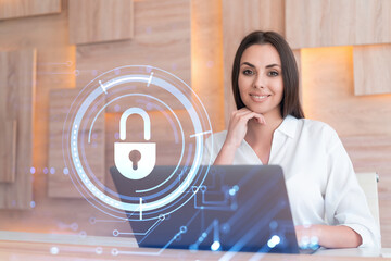 Attractive businesswoman in white shirt at workplace working with laptop to defend customer cyber security. Concept of clients information protection. Padlock hologram over office background.