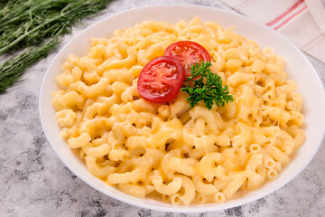 Macaroni and cheese on a white plate with parsley and cherry tomatoes on a gray background