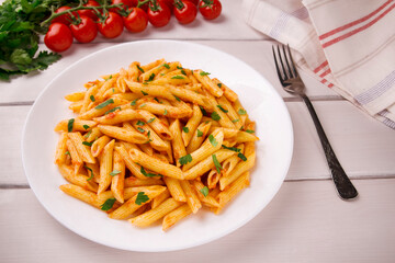 Penne pasta in tomato sauce, decorated with parsley on a white wooden table