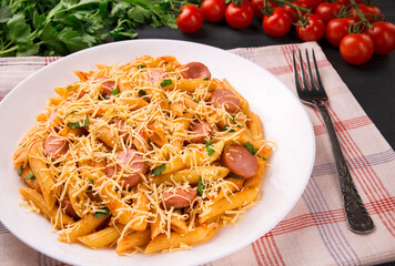 Penne pasta in tomato sauce with sausages and cheese, decorated with parsley on a  black background