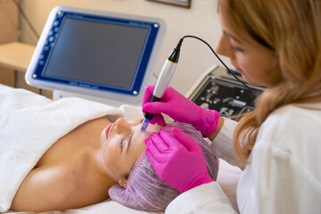 Beautician makes skin care procedure on a  face. Woman in a spa salon on cosmetic procedures for facial care. Cosmetologist making a woman a therapeutic laser processing on a face..