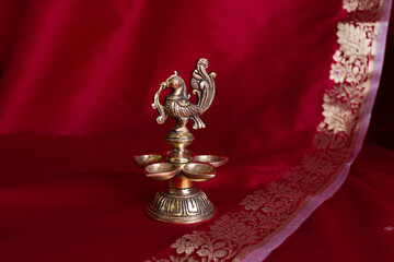 Indian traditional bronze oil lamp in the form of a bird on the background of a dark red sari....