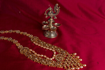 Indian traditional bronze oil lamp in the shape of a bird and gold Indian female jewelry on the red saree background. traditional Indian religious ceremony of Hindus. Diwali