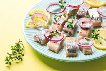 Salted herring with spice, herbs and onion on plate on yellow background with copy space. Marinated sliced fish. Food with healthy unsaturated fats, Omega 3. Top view, flat lay