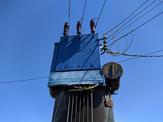 old and blue metal transformer on a pole with electric wires against a blue sky