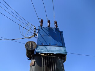 old and blue metal transformer on a pole with electric wires against a blue sky