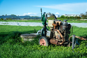Obraz premium agricultural irrigation system with an old rusty diesel water pump. Farmland scene with greenhouses in the background