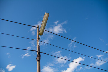 A street lamppost with wires. Wooden pole with a lantern and electric cables against a blue sky.