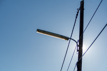 A street lamppost with wires. Wooden pole with a lantern and electric cables in silhouette against...