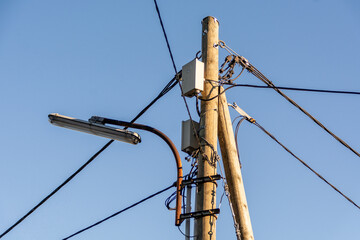 A street lamppost with wires. Wooden pole with a lantern and electric cables against a blue sky.