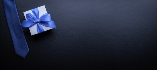 Fathers gift. White box with bow ribbon, blue bowtie or tie on dark background. Concept of Fathers Day greeting card, copy space for text.