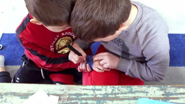 Two caucasian boys brother playing with markers, painting each others hands at home during quarantine in Greece, 4k 30fps