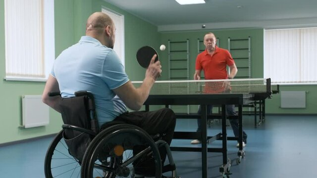 A man in a wheelchair plays ping pong. People with disabilities play table tennis. Rehabilitation of the disabled. Sport.