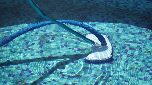 Vacuuming the dirty bottom of a swimming pool. A special brush with a striped hose cleans the pool. Hose of cleaning machine working in pool under water.