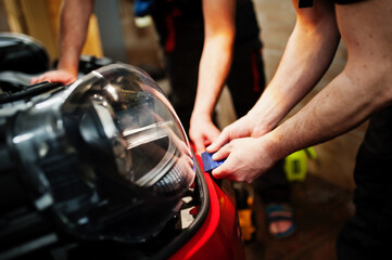Car service worker put anti gravel film on a red car body at the detailing vehicle workshop. Car protection with special films.