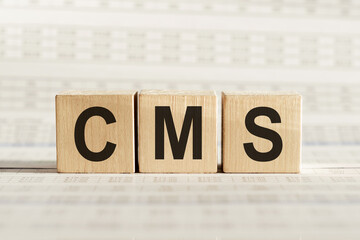 CMS abbreviation - content management system, on wooden cubes on a light background.